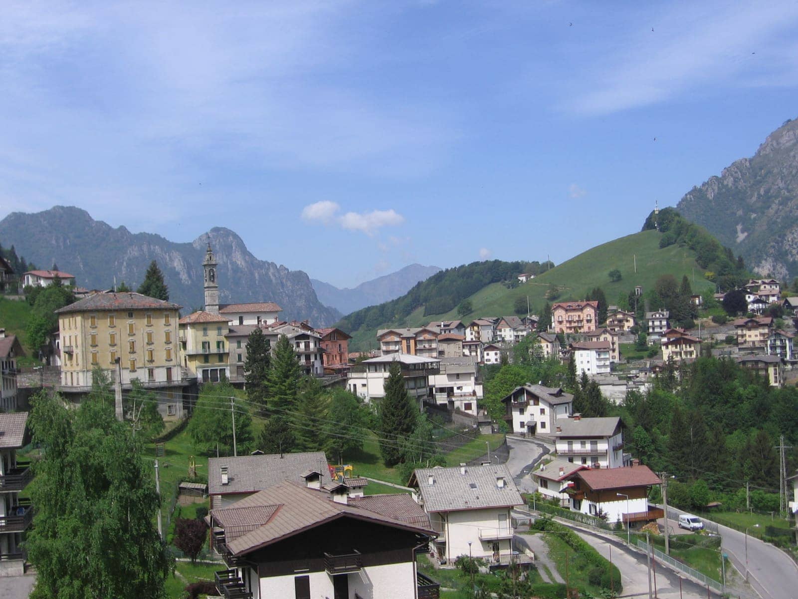 Le case e il campanile di Oltre il Colle sui prati, con le cime rocciose della conca sullo sfondo